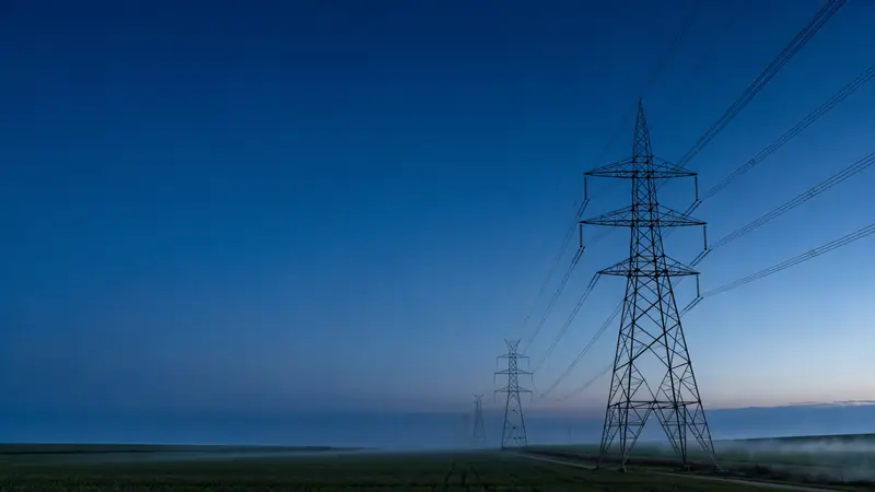 Overhead line route with lattice towers across a field at blue hour