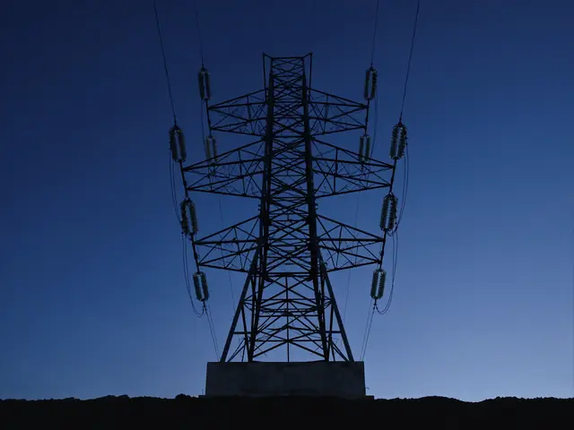 Lattice tower with insulator strings on a concrete foundation against a dark blue sky
